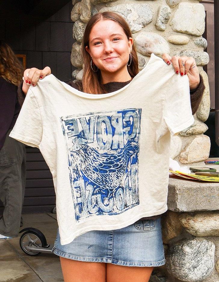 an alum holds up a shirt with an image of the grove house printed on it